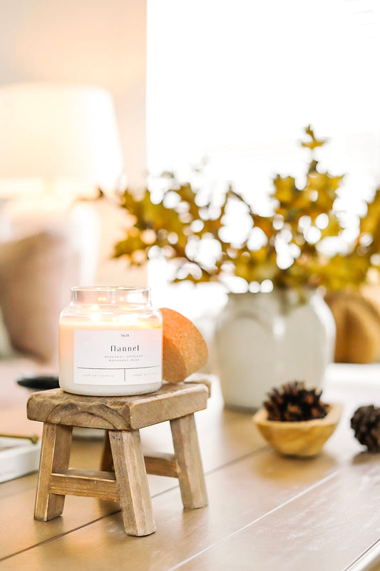 Flannel-scented 22 oz soy wax candle with cork lid, hand-poured and placed on a wooden stool in a cozy, autumn-inspired home decor setting. Clean-burning, non-toxic candle perfect for eco-friendly living and seasonal ambiance. Man Smelling Candle