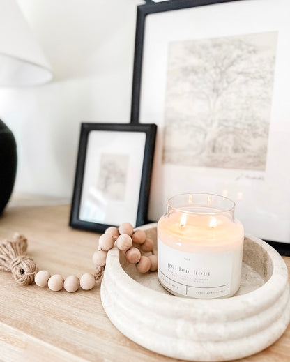 Golden Hour 100% soy wax candle with a minimalist white label, glowing warmly on a wooden table, styled with natural wooden beads in a cozy, modern home decor setting. Hand-poured, non-toxic candle ideal for creating a calming ambiance.